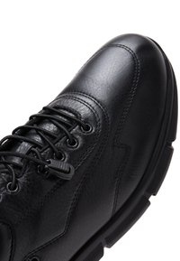 Scarpa in pelle nera con punta arrotondata, superficie texture e sistema di allacciatura. Presenta una suola in gomma e dettagli di cucitura discreti lungo i lati.