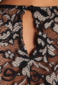 Tissus en dentelle florale noire avec une ouverture en forme de clé au dos, comportant une petite fermeture à bouton noir. Texturé avec des motifs floraux complexes.