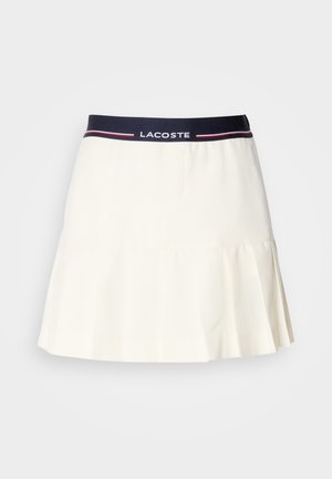 Gonna plissettata bianca con una vita blu navy, caratterizzata dal logo Lacoste e dettagli rossi. Realizzata in un materiale liscio e morbido.