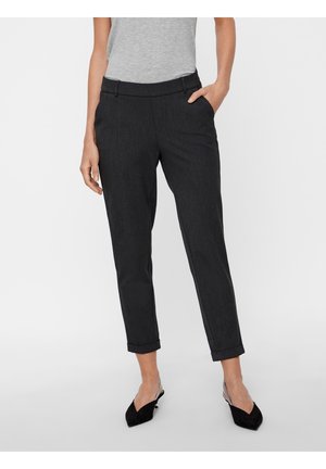 Frau trägt schlanke schwarze, knöchellange Hose mit umgeschlagenen Säumen, kombiniert mit schwarzen Slingback-Pumps und einem grauen ärmellosen Oberteil.