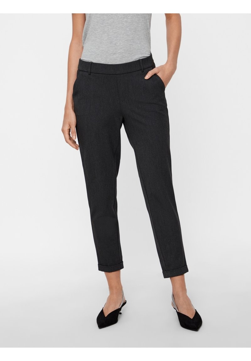 Femme portant un pantalon noir moulant longueur cheville avec ourlets retournés, associé à des escarpins noirs à bride arrière et un haut sans manches gris.