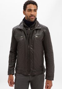 Veste en cuir marron foncé avec une fermeture éclair sur le devant, deux poches sur la poitrine et un col haut. Texture lisse avec des détails de couture visibles.