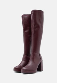 Μπορντό δερμάτινες μπότες που φτάνουν πάνω από το γόνατο με φαρδιά τακούνια, πλαϊνό φερμουάρ, λεία υφή και άψογη σχεδίαση χωρίς ραφές.