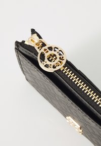 Portafoglio nero con zipper, superficie testurizzata, accessori dorati e una zip circolare con un design intagliato.