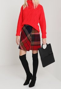 Červený pletený svetr s vysokým límcem, károvaná minisukně v červených a černých tónech, černé kozačky nad kolena a černá kabelka.