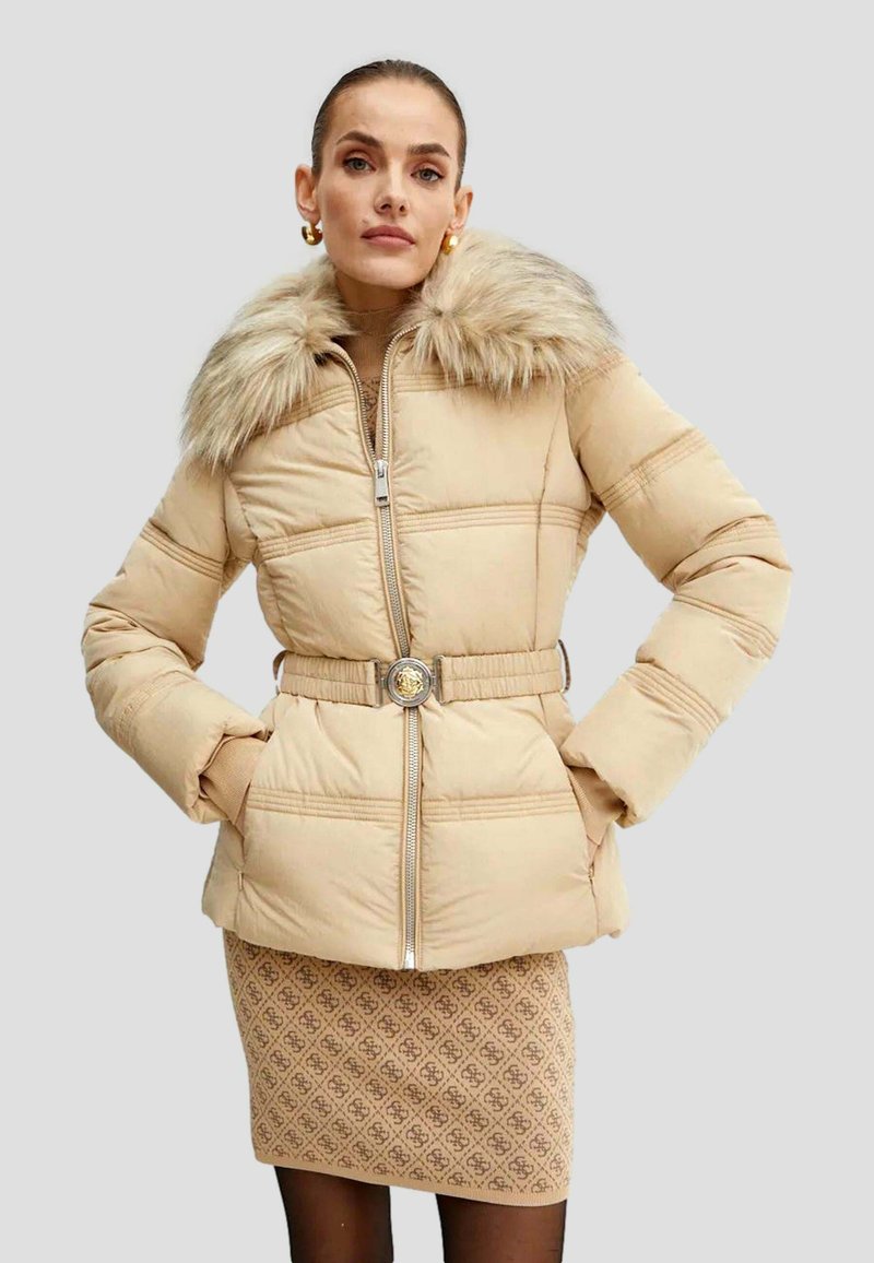 Beige pufferjakke med faux fur krave, bælte i taljen og lynlås. Kombination med en mønstret strikket nederdel og strømpebukser.