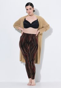 Leggings a motivo nero e rosso con accenti metallici, abbinati a un cardigan beige. Il tessuto presenta un aspetto texturizzato e una vestibilità aderente.