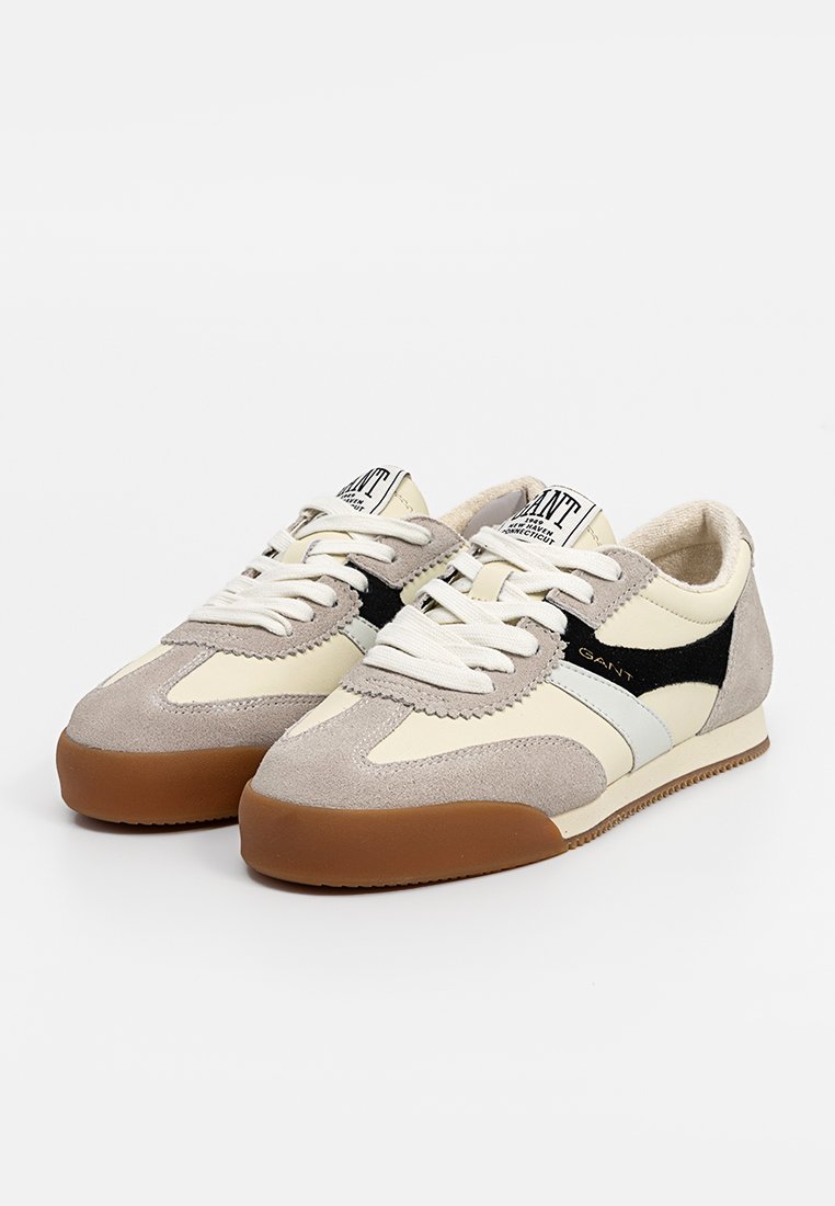 Beżowe i szare sneakersy wykonane z zamszu i skóry, z czarnym akcentem, białymi paseczkami i brązową gumową podeszwą.