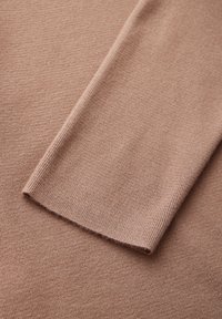 Ljust brunt stickat tröjtyg med ribbad textur och slät finish, med en platt, vikt ärm som ligger på en slät yta.