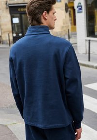 Felpa blu navy con collo alto e texture morbida, caratterizzata da una vestibilità comoda e spalle scese. Design semplice, senza loghi visibili.