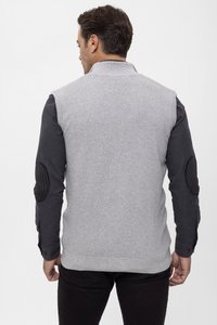 Gilet grigio lavorato a maglia con motivo testurizzato e colletto, indossato su una camicia a maniche lunghe scura con toppe nere sui gomiti. Pantaloni neri attillati.