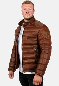 Bruine leren pufferjack met een staande kraag, ritssluiting aan de voorkant en drie zakken; beschikt over een textuurdetail op de schouders.