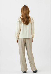 Blusa crema con dettagli in pizzo decorativo sulle maniche, abbinata a pantaloni ampi a righe grigio chiaro e scarpe nere. Outfit casual visto da dietro.