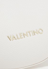 Vit läderprodukt med texturerad yta och präglad guld "VALENTINO" logotyp. Ren design med en slät finish och subtila accenter.