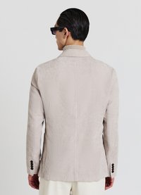 Beige Cord-Blazer aus Cord mit strukturierten Streifen, schlanker Passform, nichtchigem Revers und schwarzen Knöpfen an den Manschetten. Rückansicht, keine sichtbare Markenkennzeichnung.