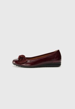 Burgundy flat shoe with a glossy patent finish, featuring a textured bow accent on the toe, and a flexible black rubber sole.