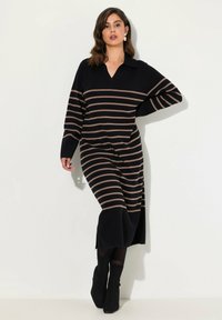 Robe midi tricotée rayée noire et fauve avec un décolleté en V et un col, dotée de manches longues et de fentes latérales, associée à des bottines noires.