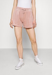Shorts en velours rose avec taille élastique et cordon de serrage, dotés d'une coupe décontractée et d'une texture douce, associés à des baskets blanches.