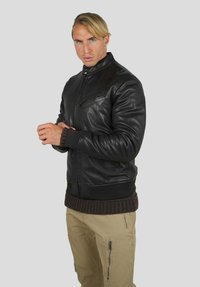 Veste bomber en cuir noir avec un col montant et une fermeture éclair à l'avant, dotée de poignets et d'un ourlet côtelés, associée à un pantalon cargo beige.