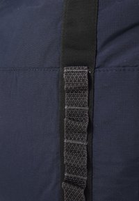Marineblauwe stoffen tas sectie met een gestructureerde zwarte webbingriem, omrandde stiksels en een gladde afwerking, wat duidt op duurzame constructie.