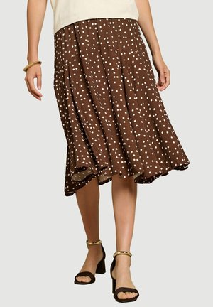 Bruine midi-rok met witte stippen, gedragen met zwarte sandalen met hak en gouden enkelbandjes, gecombineerd met een crème top en een gouden armband.