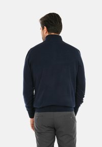 Maglione lavorato a maglia blu navy con colletto alto, polsini e orlo a coste, realizzato in un tessuto morbido. La vista posteriore mostra una superficie liscia e un design semplice.