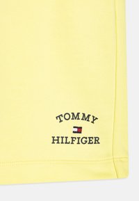 Gelbes Baumwoll-T-Shirt mit dem Aufdruck "TOMMY HILFIGER" und Logo in Schwarz und Rot, mit glatter Textur und genähtem Saum.