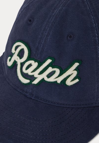 Μπλε ναυτικό καπέλο μπέιζμπολ με λευκή κεντημένη λέξη "Ralph" στο εμπρόσθιο πάνελ, περιμετρικά με πράσινο περίγραμμα, και ραμμένες τρύπες αερισμού.