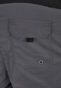 Shorts en tissu gris avec une poche arrière à rabat, accent noir et détail en œillet en métal. Texture lisse et matériau léger.