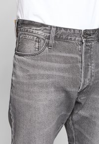 Grå denimjeans med en texturerad yta, femficksdesign och stängning med toppknapp. Har subtil blekning och färgkontraster.