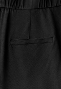 Pantalones negros con una textura suave, que cuentan con una cintura elástica y un pequeño bolsillo trasero cosido. Diseño minimalista y color sólido.
