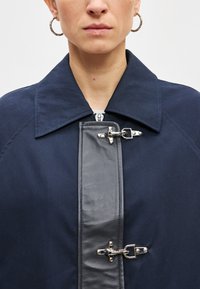 Ναυτικό παλτό με μεγάλο γιακά, διαθέτει αντίθετο γκρι πάνελ και μεταλλικά κουμπώματα στο μπροστινό μέρος. Λείο ύφασμα με δομημένο σχεδιασμό.