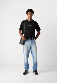 Black cotton t-shirt with white logo, light blue denim jeans, black belt, black messenger bag, and black sneakers with white stripes.