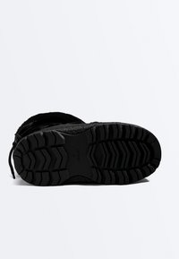Semelle d'une botte d'hiver noire avec des motifs profonds, des lacets visibles et la taille 37 imprimée sur la semelle pour l'adhérence et la durabilité.
