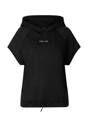 Kobieta w czapce z daszkiem, luźnej czarnej bluzie z krótkim rękawem i kapturem, czarnych spodenkach kolarskich i czarnych sandałach, stojąca na jednolitym jasnym tle.