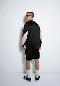 Czarny i różowy zestaw sportowy składający się z długiego rękawa bluzki o relaksującej strukturze i kontrastujących rękawach, w zestawie z pasującymi szortami i trampkami.