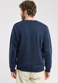 Sweatshirt bleu marine à manches longues, col rond et avec des coudières. Fabriqué en tissu doux avec des poignets et un ourlet côtelés.