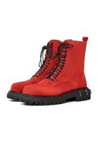 Rode suède enkelboots met zwarte veters, robuuste zwarte zool en accenten van zilverhardware. Beschikt over een ronde neus en een lusje voor gemakkelijk aan- en uittrekken.