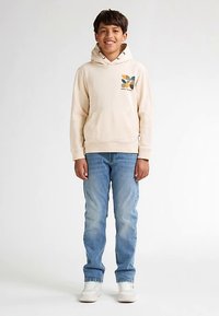 Sudadera con capucha beige con un gráfico colorido en el pecho, combinada con vaqueros azul claro y zapatillas blancas. Corte ajustado, tela suave, diseño casual.