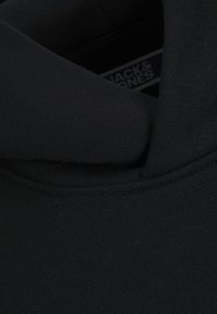 Sweat-shirt noir en tissu doux et texturé ; présente un col haut et des coutures visibles. Étiquette de marque partiellement visible à l'intérieur.