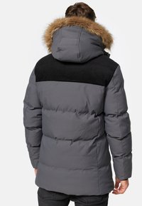 Polstret grå jakke med en sort cordurypanel på skulderen og en hætte foret med pels. Glat tekstur med en lidt oversized pasform og elastiske manchetter.