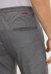 Grijze textuurbroek met een aansluitend ontwerp en elastische tailleband. Voorzien van een achterzak en een rode merketiket met de tekst "JOOP! JEANS."