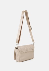 Beige kviltet håndtaske med klap, justerbar strop i stof og sølvhardware. Rektangulær form, blød tekstur.