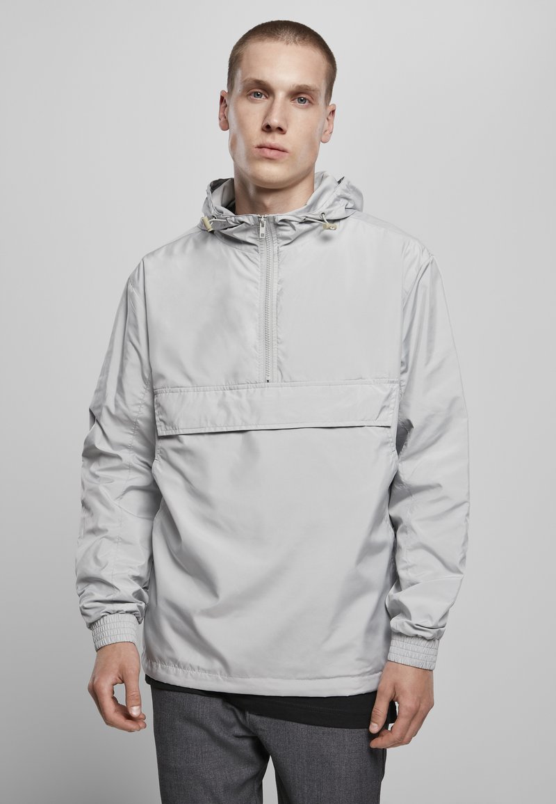 Lys grå pullover-jakke med hætte, halv lynlås foran, elastiske manchetter og en vandret brystlomme. Glat, vandafvisende stof.