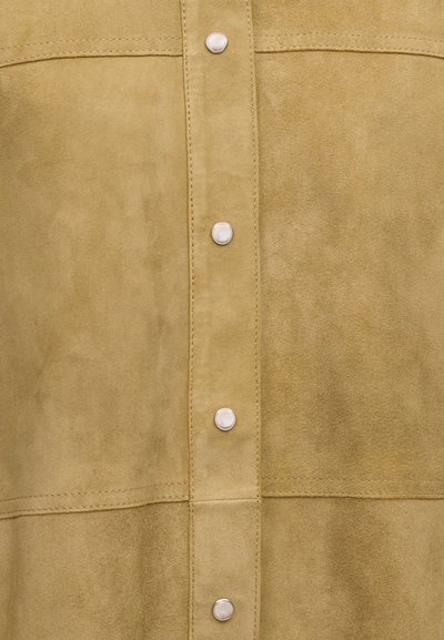 Ανοιχτό καφέ ύφασμα σουέντ με κάθετη και οριζόντια ραφή, με μια σειρά από ασημένια κουμπιά στο κέντρο.