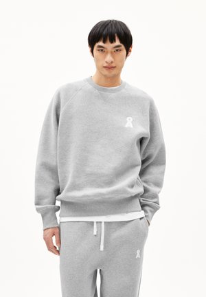 Sweatshirt gris en tissu doux, présentant un col rond et des manches raglan, avec un petit logo en ruban blanc sur la poitrine.
