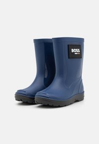 Une paire de bottes de pluie en caoutchouc bleu avec des semelles noires et un patch logo "BOSS" sur le côté, inclinées pour montrer les vues avant et latérale.
