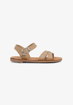 Tan læder sandal med åben tå, krydsende stropper og en metalspænde på ankelstroppen. Flad sål med let stikning.
