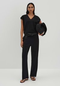 Zwarte v-hals top en brede broek, gecombineerd met een gevlochten riem en een geweven zwarte hoed. Soepele stof met een minimalistisch ontwerp.