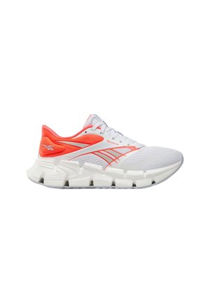 Witte sportschoen met oranje accenten, mesh bovenwerk, dikke gesegmenteerde zool en Reebok-logo aan de zijkant en hiel.